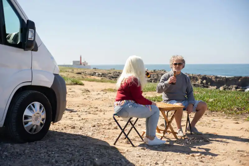 Couple en camping-car stationné sur une plage portugaise, déjeunant en extérieur