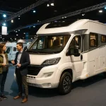 Camping-car exposé dans un salon en 2025 avec visiteurs et stands