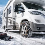 Chaînes neige installées sur un camping-car stationné sur une route de montagne enneigée en hiver