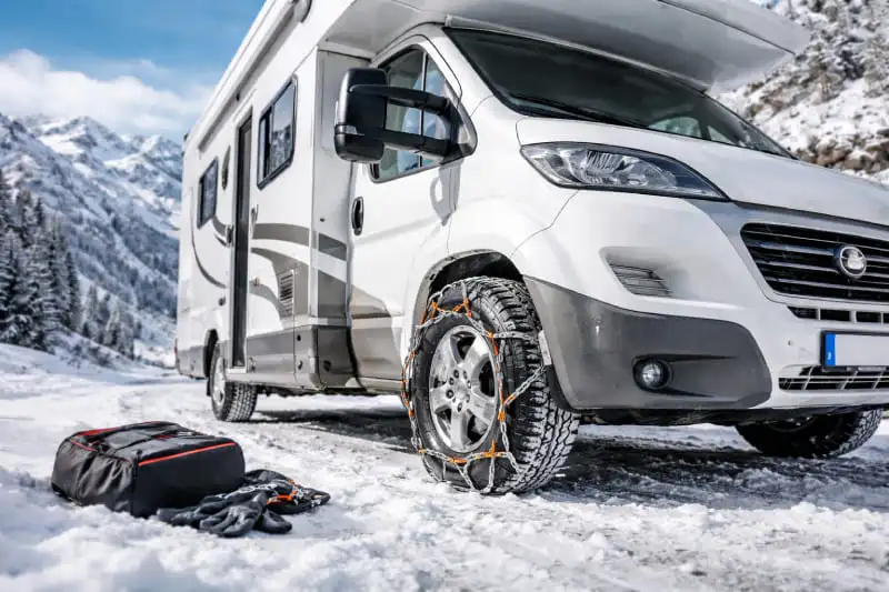 Chaînes neige installées sur un camping-car stationné sur une route de montagne enneigée en hiver