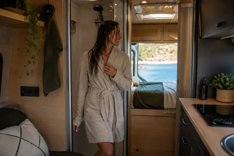 Personne sortant d’une cabine de douche à l’intérieur d’un van aménagé avec salle de bain compacte
