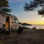 Camping-car stationné face à la mer au coucher du soleil, illustrant la vie en camping-car à l'année.