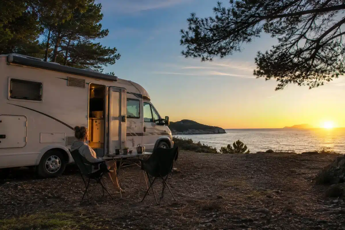 Camping-car stationné face à la mer au coucher du soleil, illustrant la vie en camping-car à l'année.